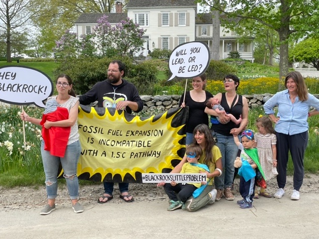 Families in front of Larry Fink's house hold signs saying "will you lead or be led" and "fossil fuel expansion is incompatible with a 1.5°C pathway", the small children are dressed in super hero outfits.