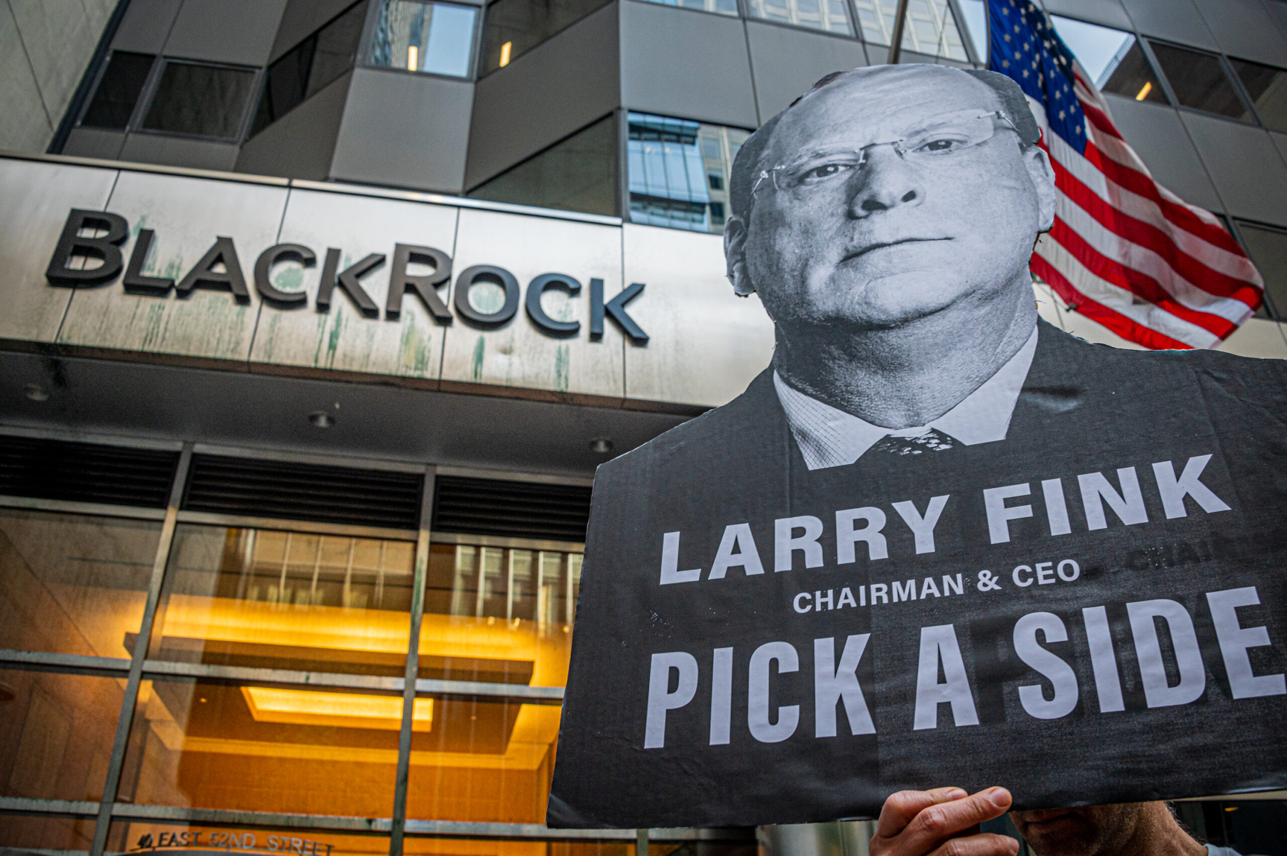 An activist holds a sign reading "Larry Fink: Pick a side" outside BlackRock's New York City headquarters.